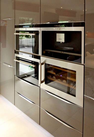 Ensemble d'appareils électroménagers encastrés en acier inoxydable dans une cuisine moderne avec armoires gris foncé et sol clair.