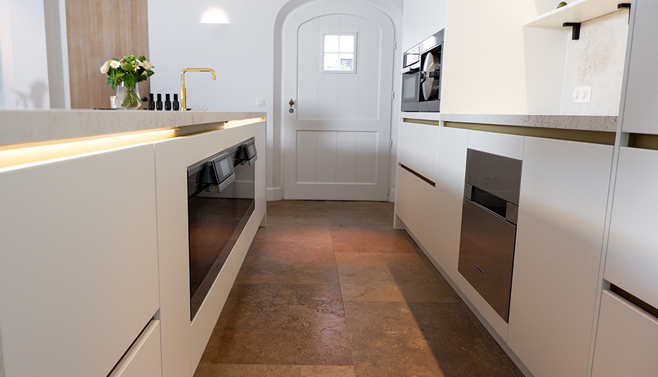 Cuisine moderne avec armoires blanches, plan de travail en pierre, robinet doré, four encastré et vase de fleurs sur le comptoir.