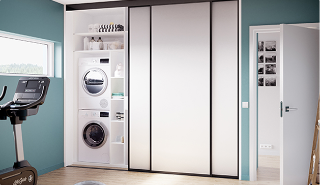 Machine à laver et sèche-linge blancs encastrés dans une armoire blanche, à côté d'un vélo d'appartement noir dans une pièce aux murs verts.