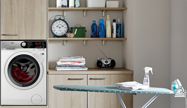 Une machine à laver blanche est intégrée dans un meuble en bois clair, avec des étagères contenant des produits d'entretien et une horloge.