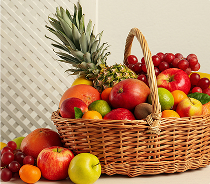 Panier en osier rempli de fruits variés, dont ananas, pommes, oranges, kiwis, raisins rouges, citron vert et mandarines, sur fond clair.