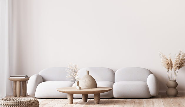 Un canapé blanc est entouré de tables en bois avec des vases décoratifs, sur un sol en parquet clair.