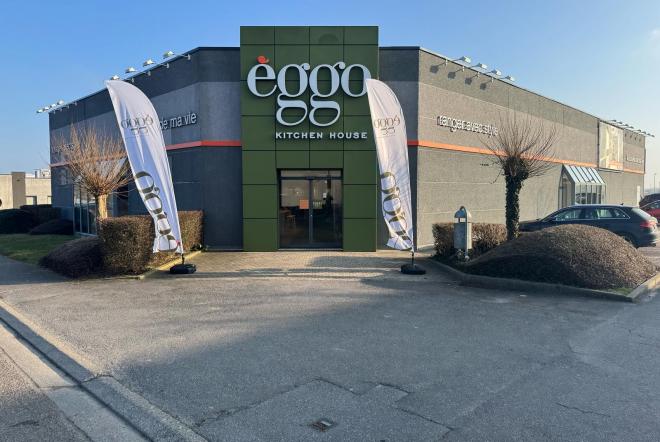 Façade du magasin èggo Kitchen House avec deux drapeaux blancs à l'entrée, bâtiment gris et vert.