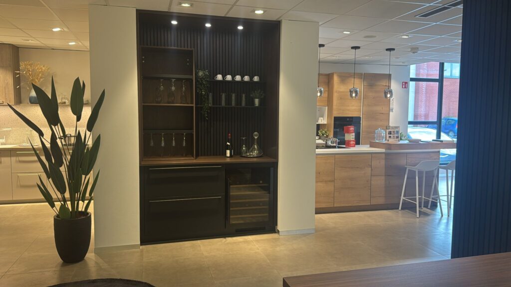 Cuisine moderne avec des armoires en bois clair, un comptoir blanc, une étagère avec des verres et une plante verte en pot.