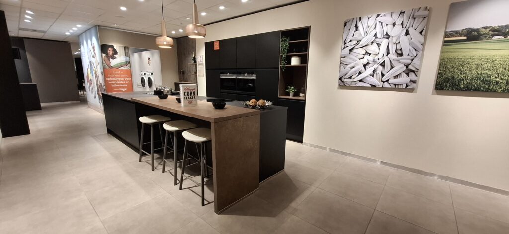 Cuisine moderne avec îlot central en bois, tabourets blancs, et armoires noires, décorée de deux suspensions et des tableaux muraux.