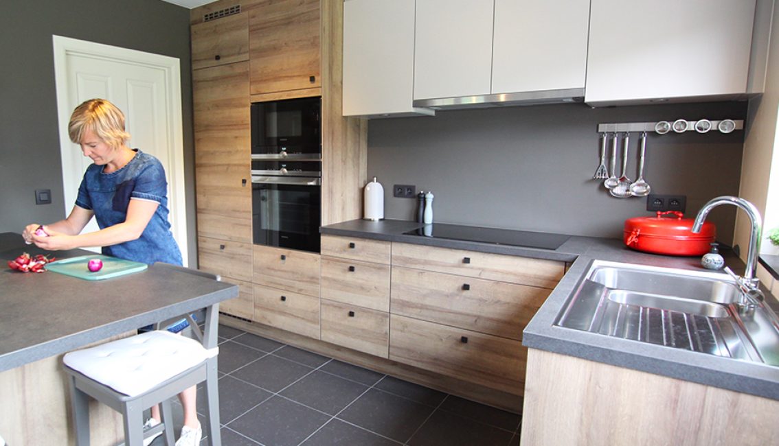 Une femme épluche des oignons rouges dans une cuisine moderne avec des armoires en bois clair et un plan de travail gris.